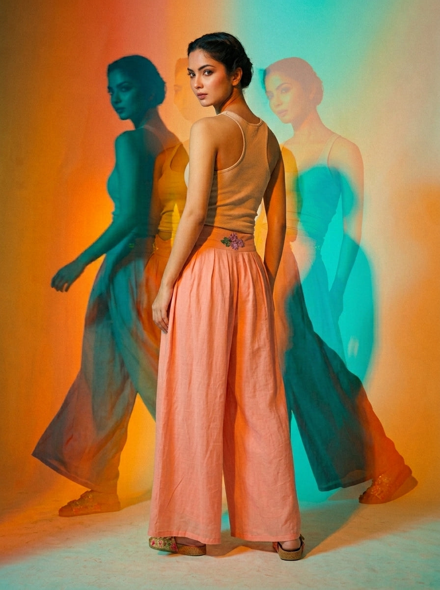 Woman modeling wide-legged coral pink trousers with a flowing sheer overlay and a fitted brown top, shown from multiple. - Pantalon BLOOM - S - ALTER EGO