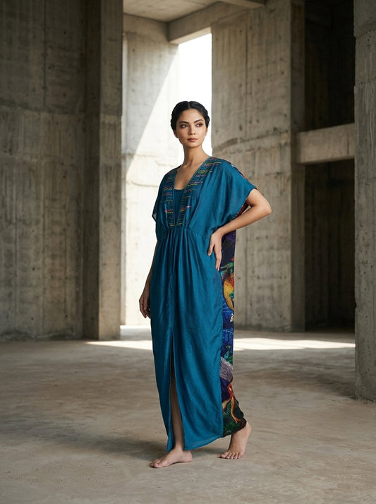 Woman wearing a flowing teal-blue caftan with a V-neck, short sleeves, and colorful floral side panels. - Caftan EDEN - S - ALTER EGO