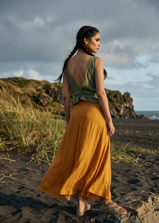 Woman wearing a flowing saffron-orange maxi skirt with a sleeveless olive top on a rocky beach. - Jupe DOVE - S - ALTER EGO